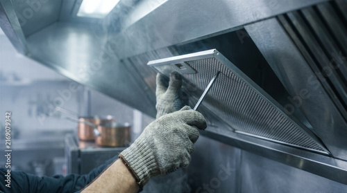 Professional worker wearing protective gloves cleaning and maintaining a commercial kitchen exhaust hood filter in a restaurant