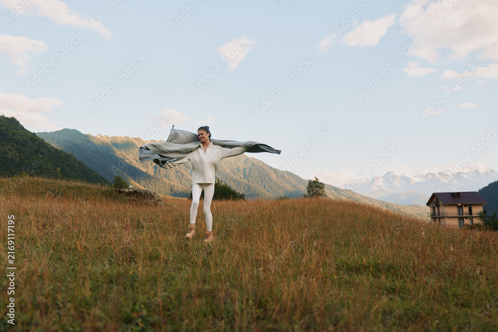 Naklejka premium Man in white clothes stands in a grassy field with a scarf spread wide, enjoying the outdoors, bright day, distant mountains, sense of freedom and adventure