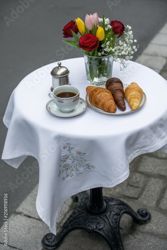 Small round cafe table with fresh croissants, coffee and a bouquet of flowers