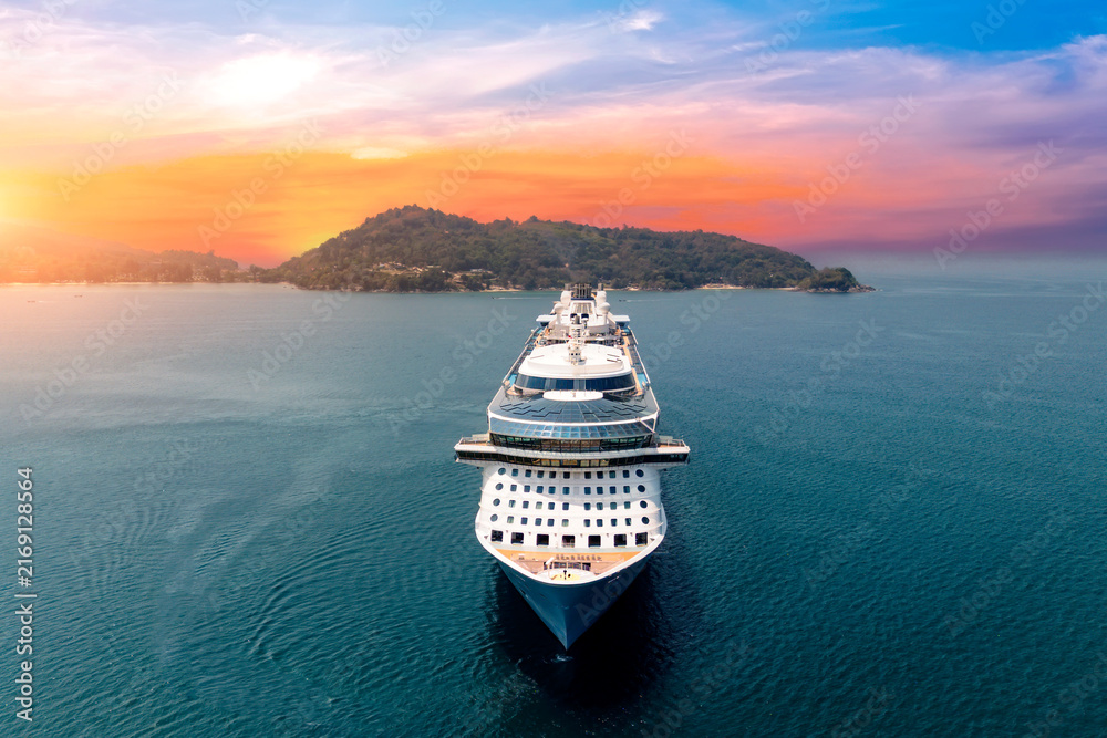Obraz premium Aerial straight view typical cruise ship sailing on the ocean during a golden summer sunset with islands and mountains in the background.