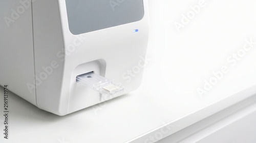 Compact medical device with diagnostic sample cartridge loaded on sterile white table, advanced healthcare diagnostics technology concept.