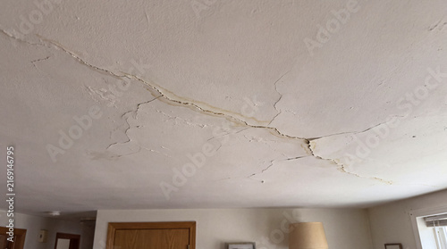 Photograph showing extensive cracks and unsightly water damage spreading across a white interior ceiling due to.