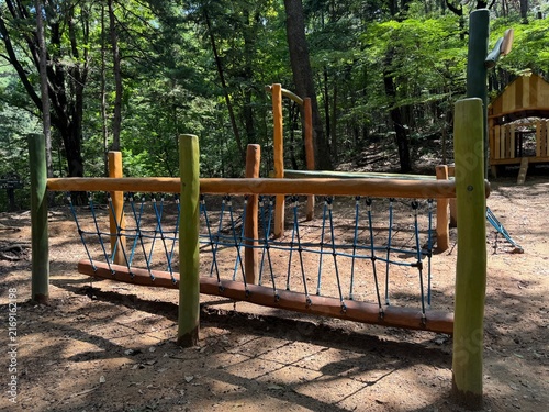 Wooden rope bridge and playhouse at shaded outdoor forest playground