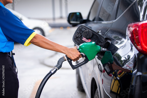 Obraz na płótnie Close-up of a gas station attendant holding a green fuel nozzle to refuel a black car at a petrol station during daytime