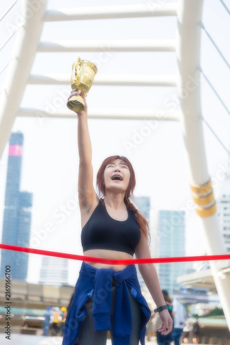A beautiful, fit woman holds a victory trophy in the middle of the city; a concept promoting health.