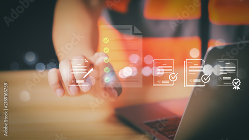 Engineer touching virtual quality checklist and document icon on laptop screen for paperless business management and digital compliance approval workflow.