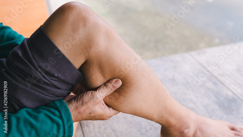 Close-up of a senior person holding their painful calf muscle outdoors. The elderly adult is suffering from acute leg cramps, muscle spasms, and physical discomfort. Medical healthcare concept.