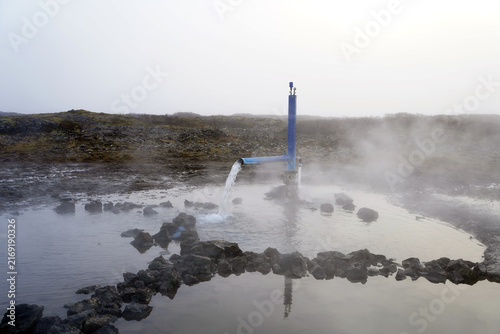 Картината върху платно A pipe pours hot geothermal water into a stone-lined thermal pool, sending steam