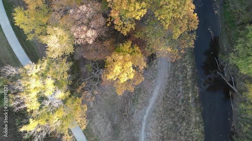 Flying up from directly overhead of a fall creek shot with a dirt path, paved multi use path and water path in Coralville Iowa with stunning fall foliage. 4k, drone, flying up, looking straight down