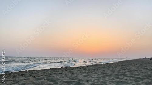 Sunset over calm sea waves and rippled sandy shore with a bird in flight, capturing serene coastal beauty, soft reflections, and peaceful atmosphere in timeless scenery