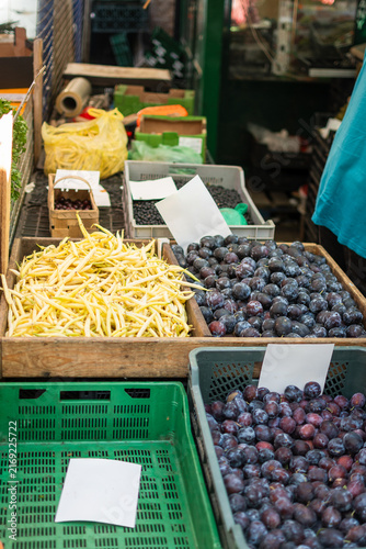 Vertical photo of yellow beans and plums on a bench at an outdoor local market.