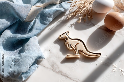 Kangaroo shaped cookie cutter on a marble surface with eggs, towel and dried flowers.