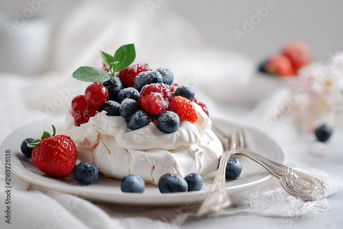 Delicate Pavlova Dessert with Fresh Berries and Mint, Presented on a White Plate with Silver Fork