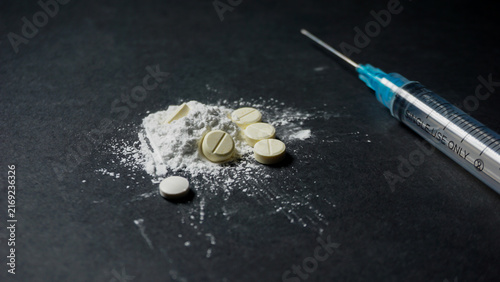 syringe and pills. Disposable medical syringe with some illegal white drugs in powder and pill form. Misused drugs concept. 