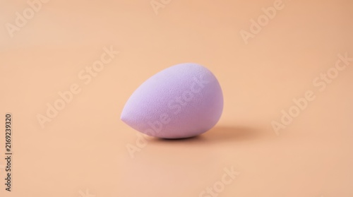 Obraz na płótnie Purple makeup sponge on a soft peach background