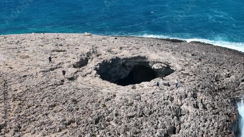 hikers explore blowhole rim coral lagoon headland malta turquoise cove visible beyond honeycomb weathered limestone drone circles overhead sinkhole natural sea cave collapse popular hiking viewpoint