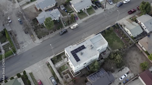 Aerial view of a quiet residential street with houses featuring solar panels and cars driving by.