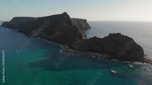 Cinematic aerial view of dramatic rocky coastline and turquoise ocean waters at sunset.