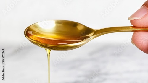 Golden oil drips from a spoon held by a hand in a kitchen setting