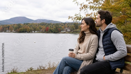 Couple sitting on bench looking at autumn lake and mountains