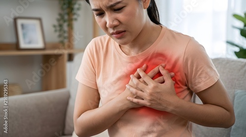 Woman suffering from acute chest pain holding her chest while sitting on a couch in the living room.