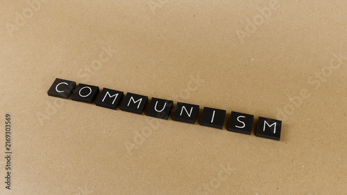 фотографія Black square tiles with white letters spelling COMMUNISM on a textured light bro