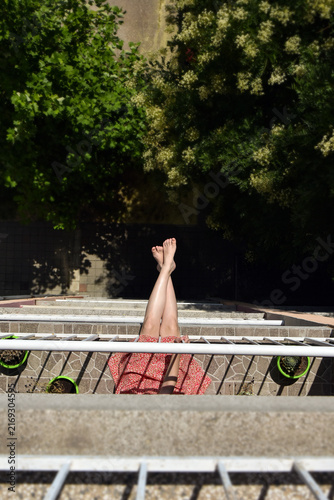 Young woman in floral dress sitting on the edge of a terrace in an apartment building, playful urban summer vibe downward view