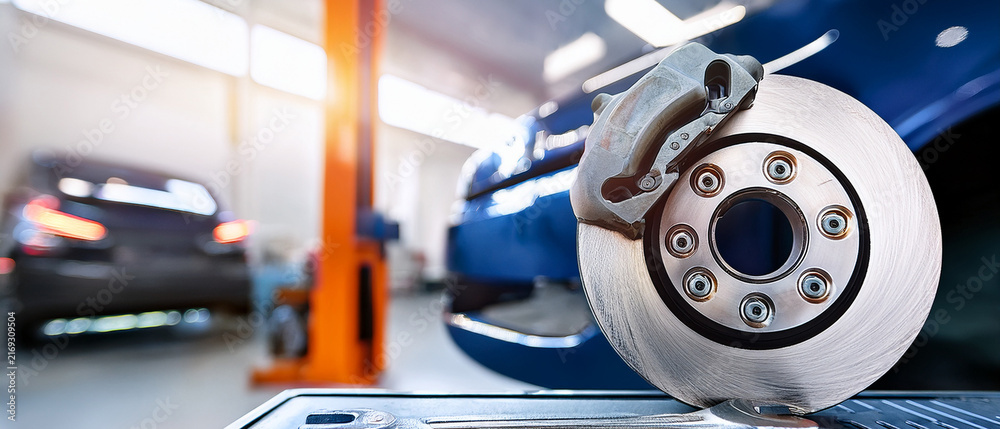 Fototapeta premium New car brake disc rotor and caliper in modern auto repair service workshop