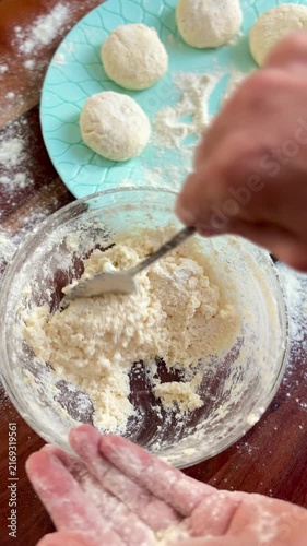 Hands shape soft cottage cheese dough into round patties on a flour-dusted wooden table to prepare traditional syrniki or pancakes.