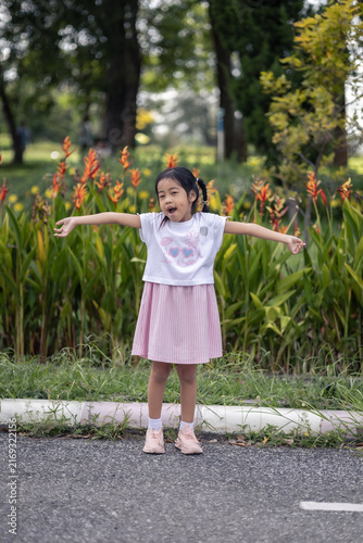 Photography A young girl is relaxing in a public park; she is standing on asphalt , waving and smiling
