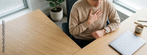 Woman sitting at office desk holding hand to chest in pain