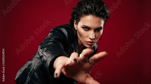 Woman in Leather Jacket Reaching Towards Camera Against Red Background