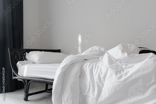 messy blanket on clean white bed and white pillow with morning light  in bedroom of house, resort or hotel, in soft focus