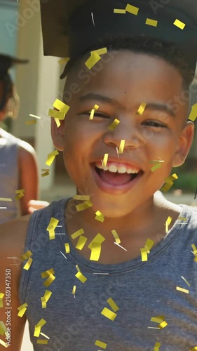 Animation of gold confetti over happy schoolboy wearing mortarboard outside school