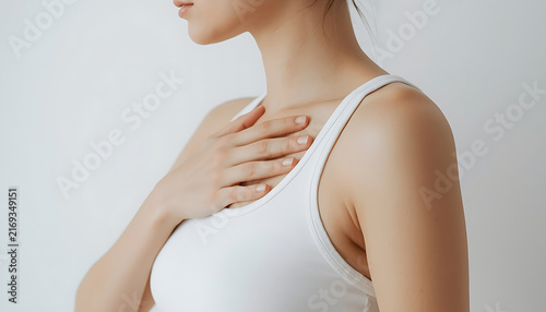 The image shows a person in a white tank top with their hand placed flat against their chest wall