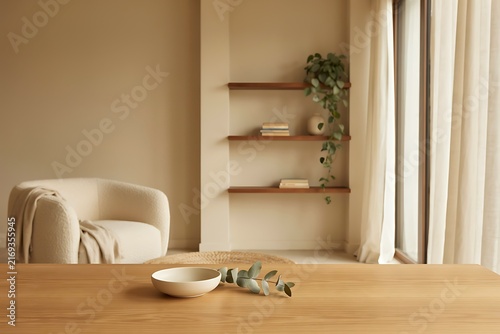 Beige armchair with throw blanket, wooden shelves with books and plant, and table with bowl