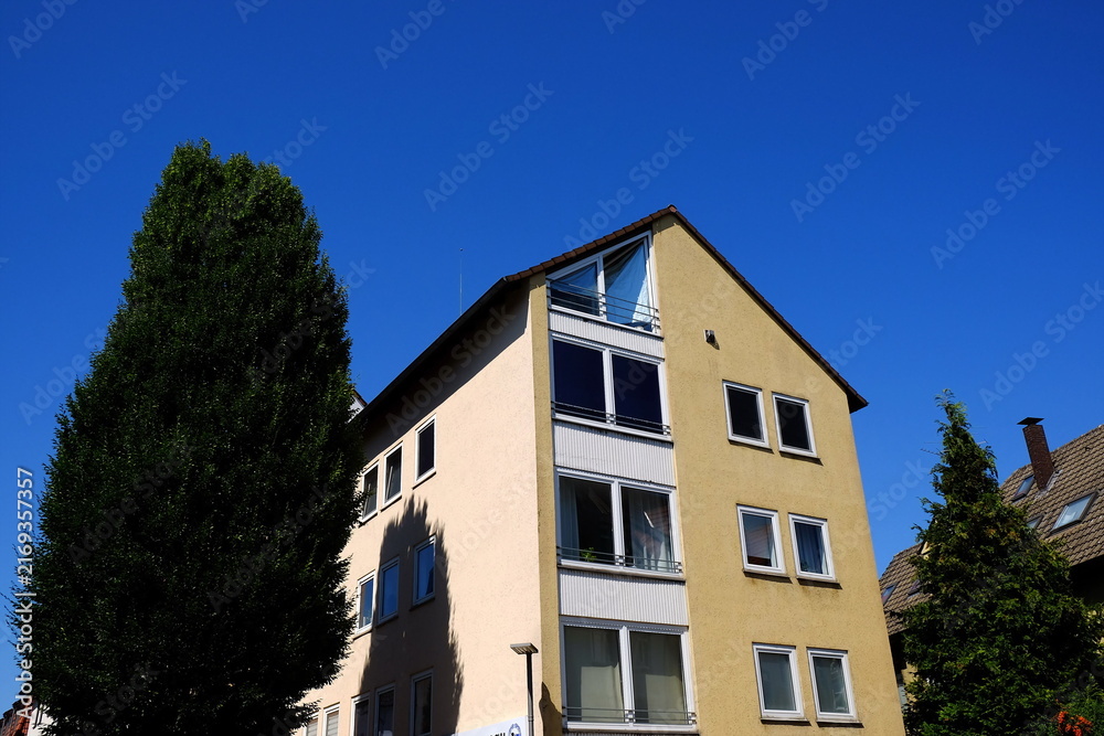 Fototapeta premium Mehrstöckiges Wohnhaus mit spitzem Giebel und Fassade in Beige und Naturfarben vor blauem Himmel bei Sonnenschein in Bielefeld im Teutoburger Wald in Ostwestfalen-Lippe