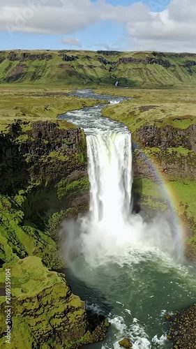 Majestic Waterfall and Rainbow in Icelandic Landscape - An awe-inspiring waterfall cascades down a rocky cliff face in Iceland, creating a mist at its base.