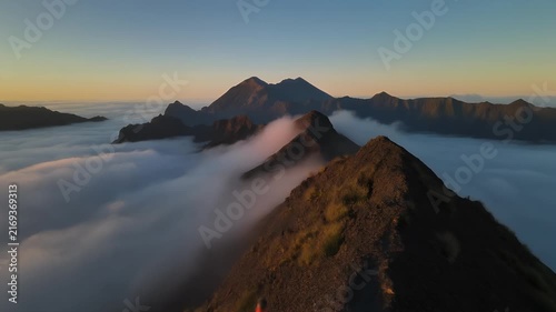 Two hikers stand on a mountain ridge at sunrise above a sea of clouds.