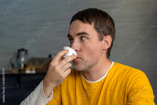 Foto Thoughtful man drinking tea from a small white bowl or cup, looking away thoughtfully