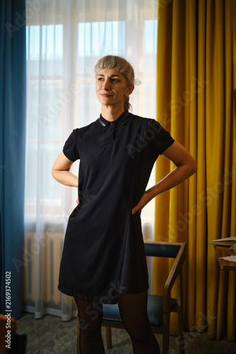 Foto Woman stands in room wearing little black dress near window with yellow curtains