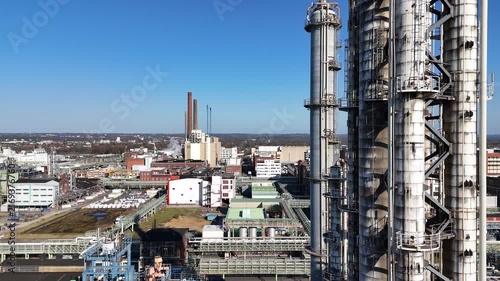 Drone climbs beside a silo tower while pipelines and buildings recede below in an upward industrial perspective.