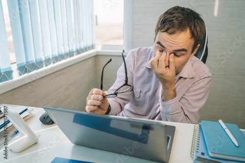 Tired remote worker in home office removing glasses and rubbing eyes, eye strain and exhaustion.