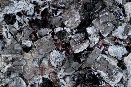 Macro close-up of smoldering charcoal pieces with glowing red embers and white ash texture after burning in a fire pit or grill