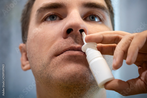 Man using a nasal spray to treat a stuffy nose and congestion, looking at the camera. Allergy relief, sinus treatment, and cold symptoms.