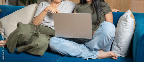 Картината върху платно Women relaxing on a blue sofa, using a laptop together at home