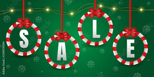 Christmas sale vector banner design with hanging baubles in candy cane style with letters S A L E on green background with snowflakes.