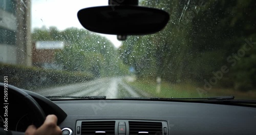 POV shot inside a car driving on a rainy road with wind blowing water droplets up the windshield glass. Wet countryside road in bad weather
