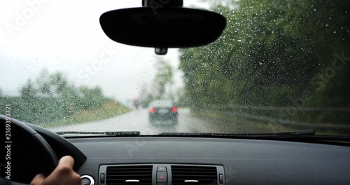 POV shot of driving car on rainy road following a vehicle with oncoming truck traffic. Driver view through wet windshield