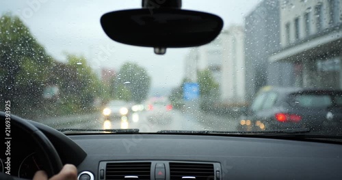 POV shot of driving car on rainy road following traffic in city. Driver view through wet windshield